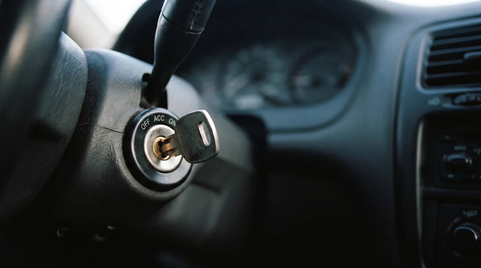 A worn silver car key partly inserted in an ignition cylinder